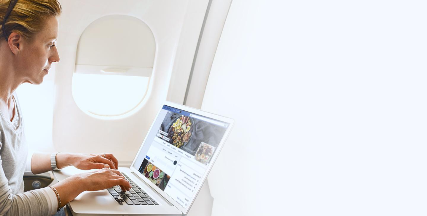 一名女子坐在飞机上，用笔记本电脑上网浏览脸谱网