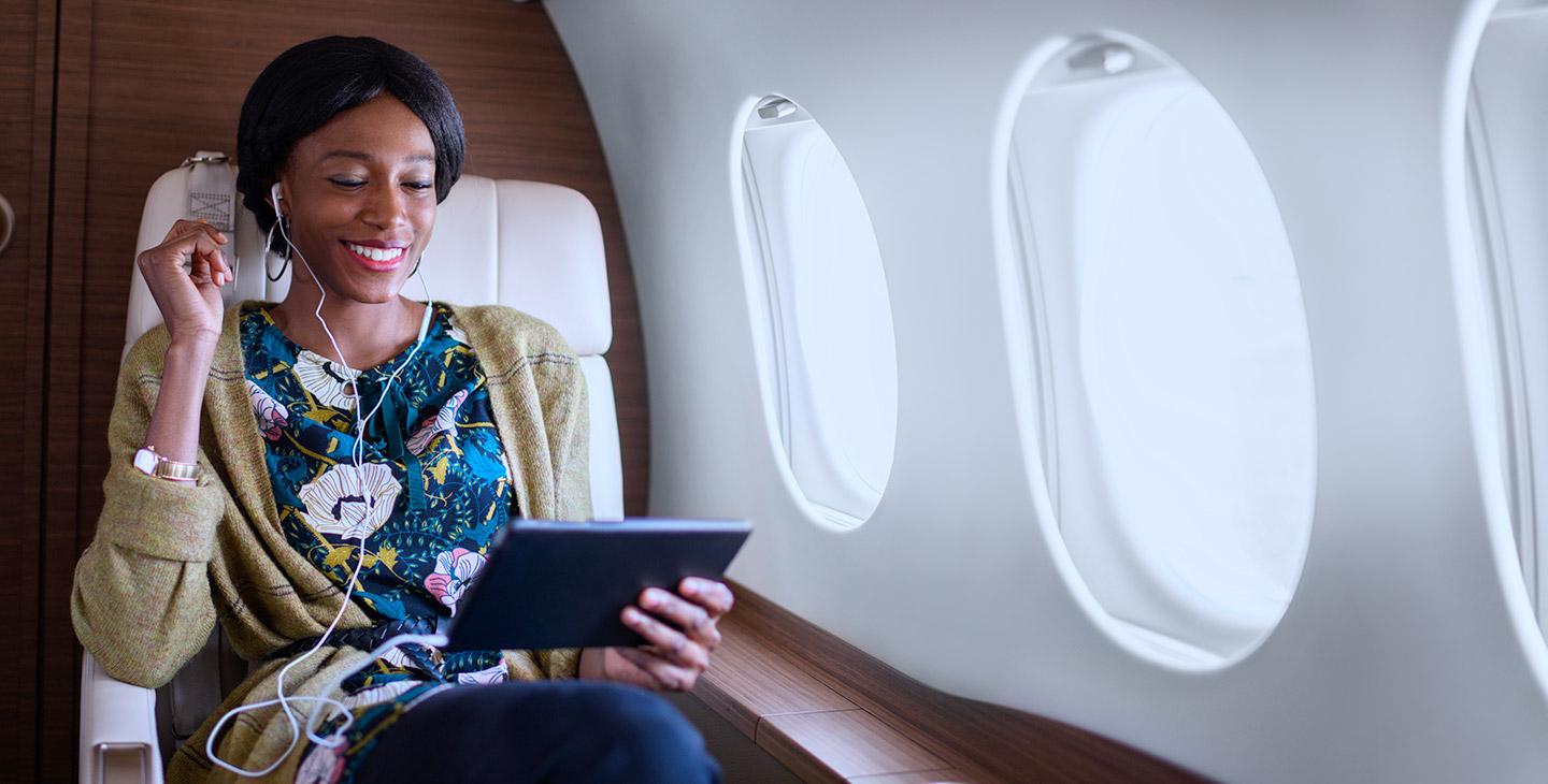 一名身穿花衬衫的女子，戴着与平板电脑相连的耳机, 在私人飞机上享受飞行娱乐