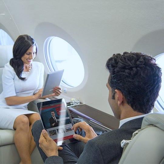 在一架私人飞机上，职业男女面对面坐着，看着平板电脑上的机上娱乐节目