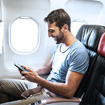 一名棕色头发的男子坐在靠窗的座位上，用智能手机上网