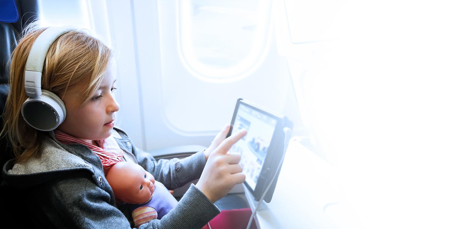 小女孩戴着耳机，腿上放着一个娃娃，在平板电脑上享受飞行娱乐