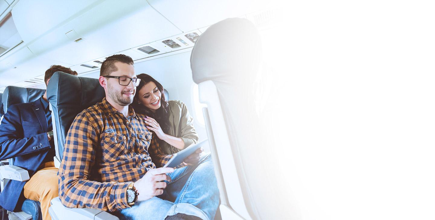 飞机上，一个男人和一个女人坐在一起，享受着飞机上的乘客体验, 看平板电脑
