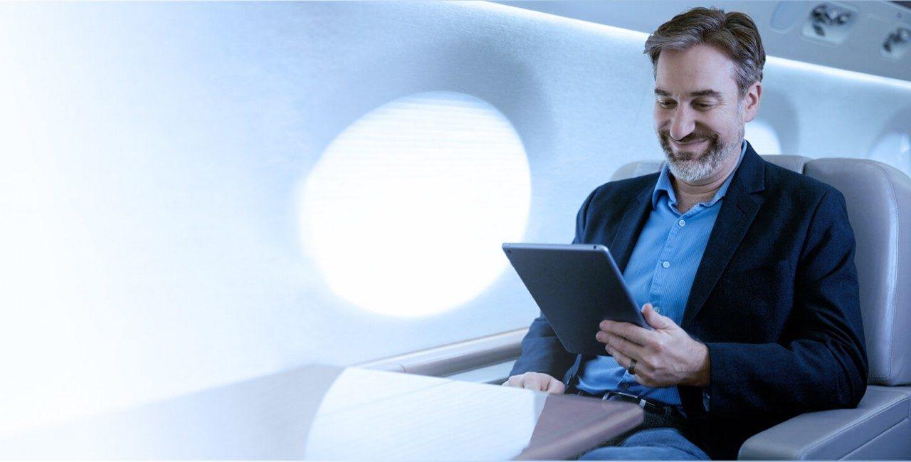 一名穿着西装外套的男子坐在一架私人飞机上，用飞机卫星互联网连接他的平板电脑