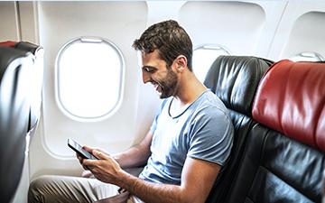 一名男性乘客坐在飞机窗边，用智能手机上网