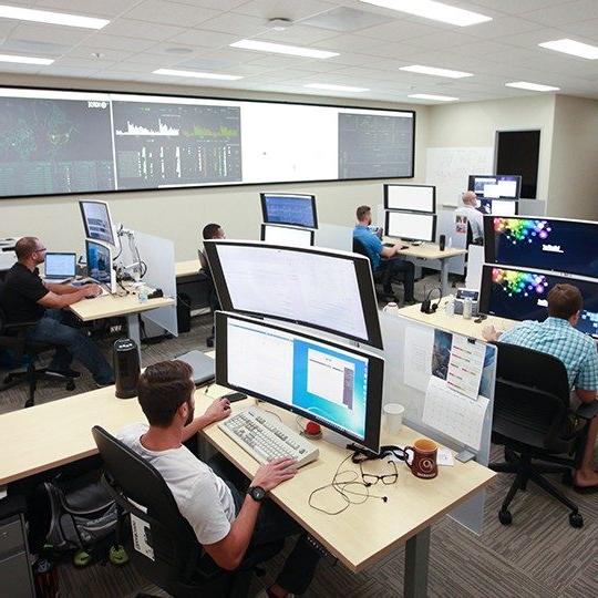 六名Viasat员工的团队坐在2个大的, 在网络安全行动中工作的堆叠监视器