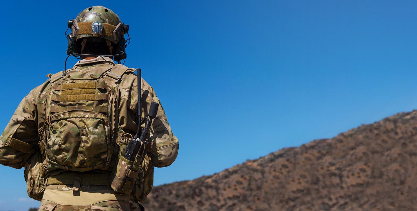 一个士兵在战场上的背影, 他的背包里装着一个带有天线的BATS-D手持收音机