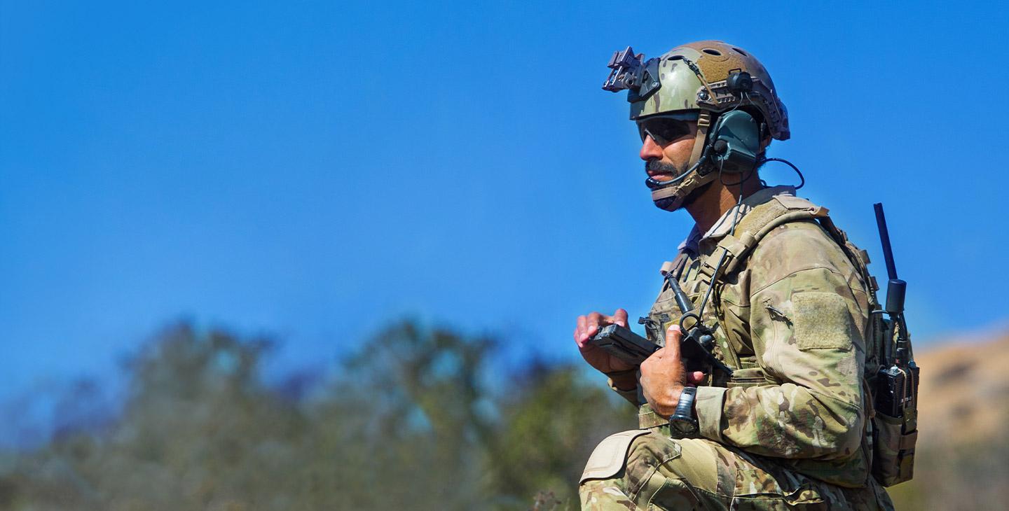 一个士兵在战场上单膝跪地的特写, 他穿着军装，背着一个装有天线的BATS-D AN / prc - 161手持收音机的背包