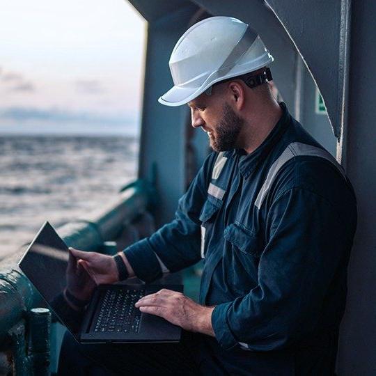 一个戴着安全帽的人在海上的船上用笔记本电脑上网.