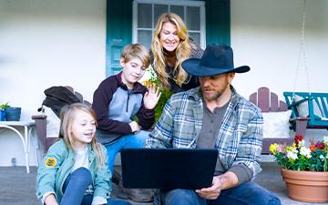一个农场主，他的妻子和两个孩子在门廊上用他们的笔记本电脑享受家庭wifi