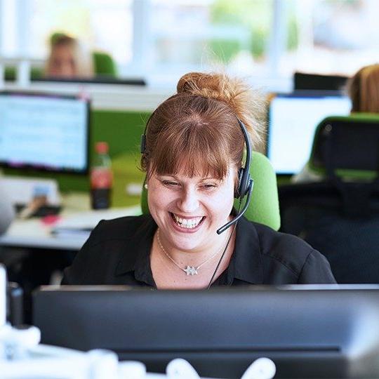 A woman working in a sales call center is smiling, talking to a customer about Viasat EasyCare