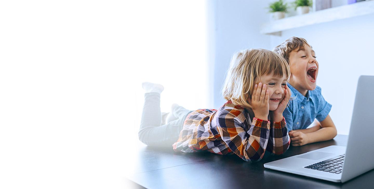 一个小女孩和一个小男孩被网络安全软件保护着，躺在地板上对着笔记本电脑笑