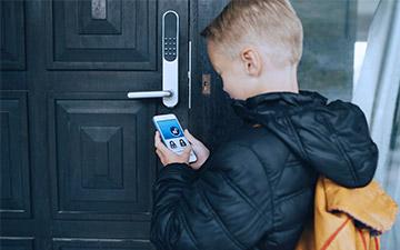 一名年轻的学生拥有家庭网络安全，他站在一扇门前，用智能锁锁住自己